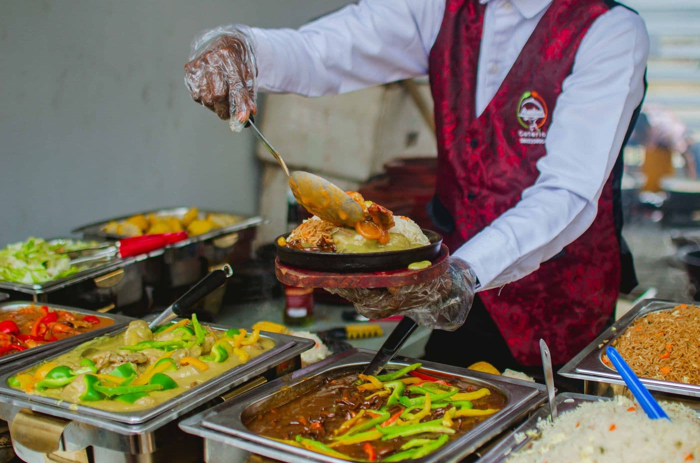 Un serveur en gilet garnit une assiette de riz et de sauce derrière les bacs du service