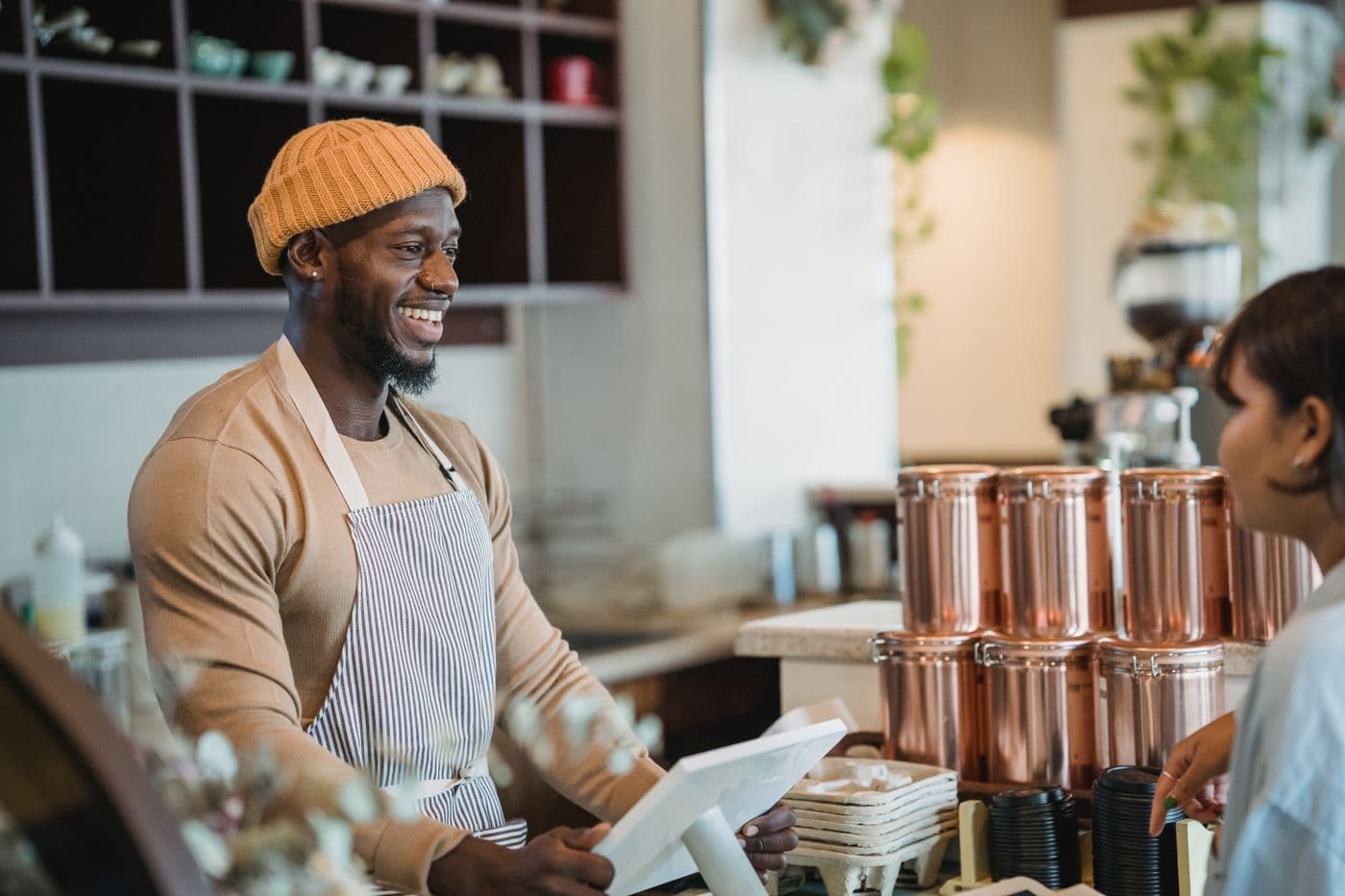Un gérant en tablier, souriant, derrière la caisse de son comptoir